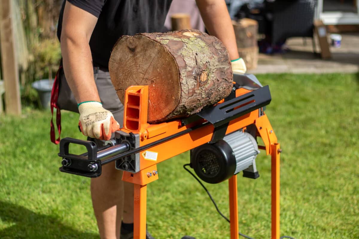 man with work gloves using an electric log splitter in garden